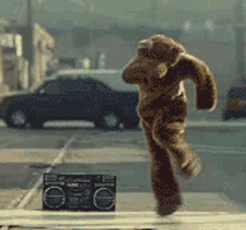 A Teddy Bear Is Running On A Street Next To A Boombox GIF