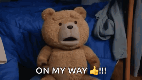 A Teddy Bear Is Sitting On A Bed And Giving A Thumbs Up Sign GIF