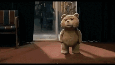 A Teddy Bear Is Standing In Front Of A Door In A Room GIF