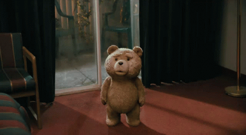 A Teddy Bear Is Standing On A Red Carpet In A Dark Room GIF