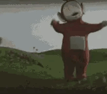 A Teletubbies Character Is Standing In A Grassy Field . GIF