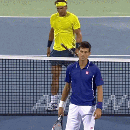 A Tennis Player In A Blue Shirt Stands Next To A Player In A Yellow Shirt On A Tennis Court GIF