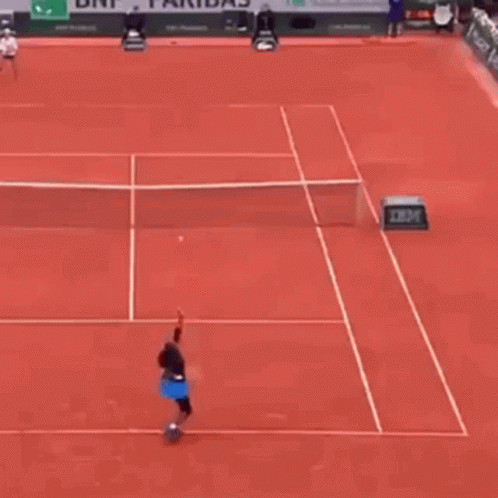 A Tennis Player Is Hitting A Tennis Ball On A Red Tennis Court . GIF