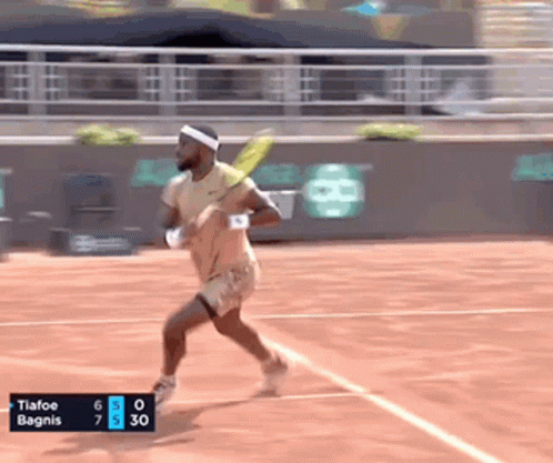a tennis player is running on a court with a scoreboard that says tiafoe bagnis at the bottom