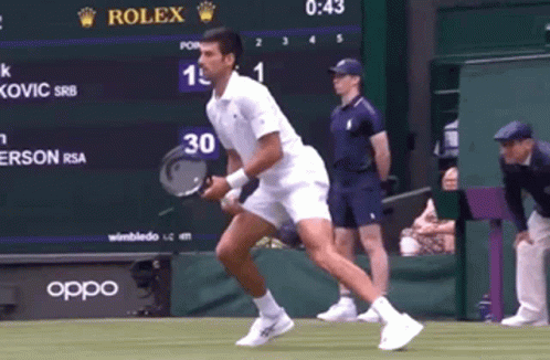 A Tennis Player Is Running With A Racket In Front Of A Scoreboard That Says Rolex On It GIF