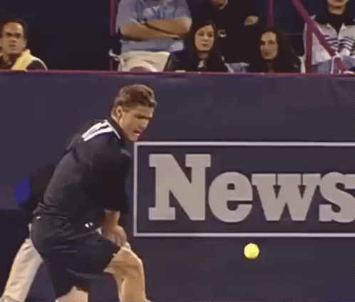 A Tennis Player Swings A Racket In Front Of A News Sign GIF