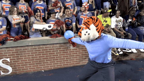 A Tiger Mascot Throws A Blue Ball In Front Of A Crowd With A Letter S In The Background GIF