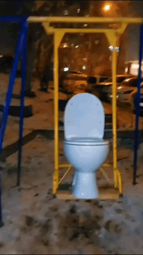 A Toilet On A Swing In A Playground At Night GIF