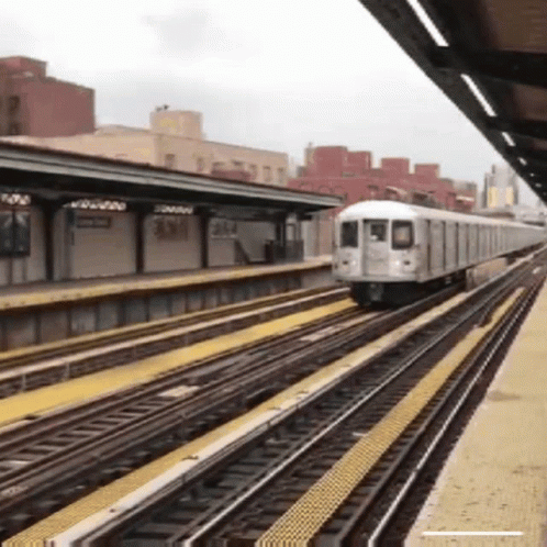 A Train Is Going Down The Tracks At A Station With A Building In The Background GIF