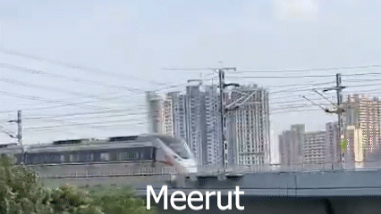 A Train Is Going Over A Bridge In Front Of A Building . GIF