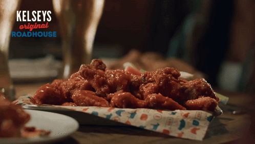 A Tray Of Chicken Wings Sits On A Table With A Sign That Says Kelseys Original Roadhouse GIF