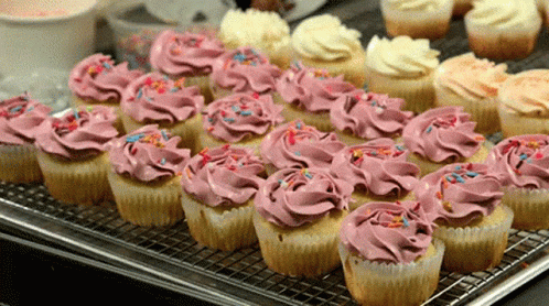 A Tray Of Cupcakes With Pink Frosting And Sprinkles On Them GIF