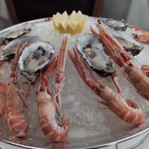 A Tray Of Oysters And Shrimp On Ice With A Lemon On Top GIF