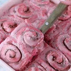 A Tray Of Pink Cinnamon Rolls With A Knife In It . GIF