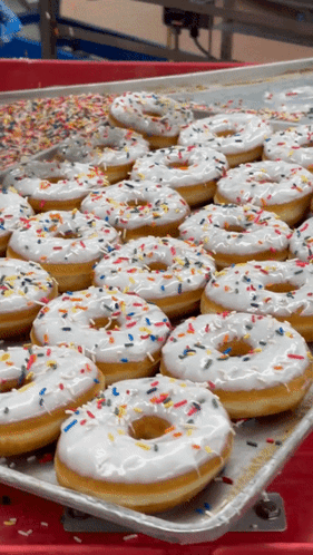 A Tray Of White Frosted Donuts With Sprinkles GIF
