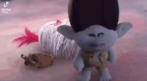 A Troll Doll Is Standing Next To A Ball Of Yarn On A Table . GIF