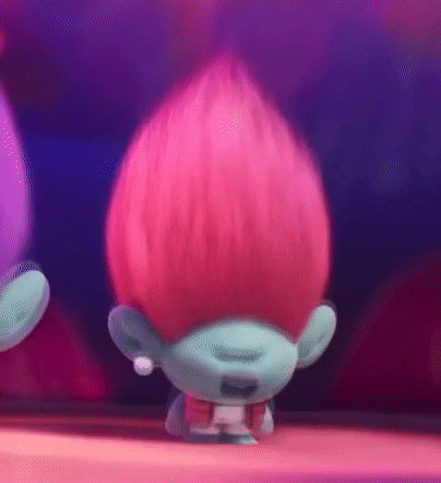 A Troll With Pink Hair And A Blue Face Is Standing On A Table . GIF