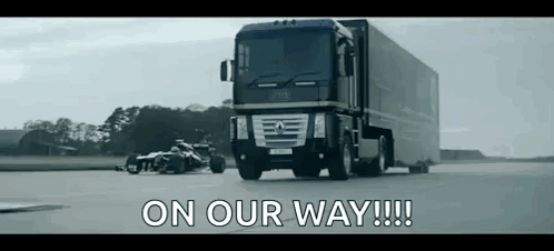 A Truck Is Driving Down A Road Next To A Race Car With The Words `` On Our Way !!! '' Written On It . GIF