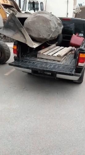 A Truck With A Large Rock In The Back Is Parked On A Street GIF