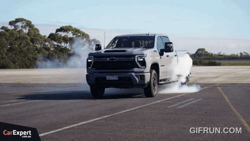 A Truck With Smoke Coming Out Of The Tires Is Driving Down A Road With A Car Expert Logo In The Corner GIF