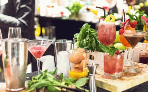 A Variety Of Drinks Are On A Table Including A Martini With Strawberries GIF