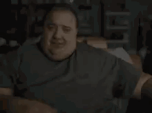 A Very Fat Man Is Sitting On A Couch In A Dark Room . GIF