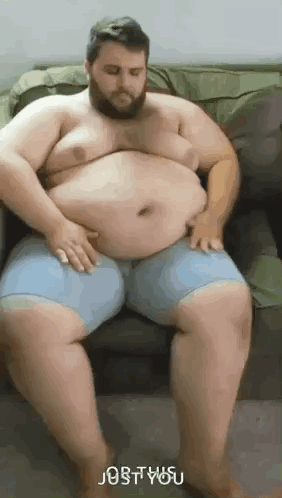 A Very Fat Man With A Beard Is Sitting On A Couch With His Hands On His Belly . GIF