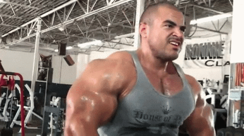 A Very Muscular Man Is Lifting Weights In A Gym Wearing A Tank Top That Says House Of Bodybuilding . GIF