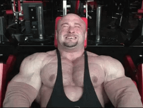 A Very Muscular Man Is Sitting On A Machine In A Gym . GIF