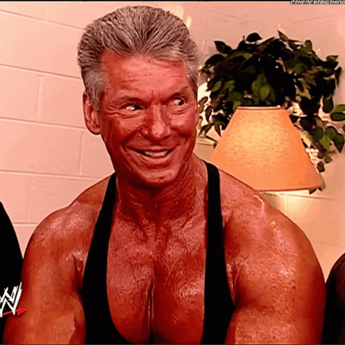 A Very Muscular Man Is Smiling And Wearing A Black Tank Top With The Letters N On It GIF