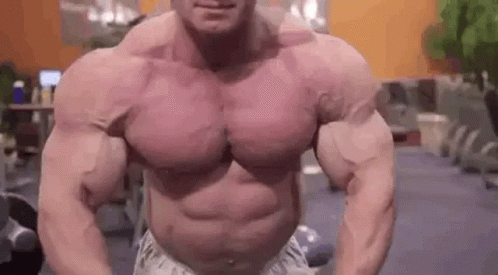 A Very Muscular Man Is Standing In A Gym With His Arms Outstretched . GIF