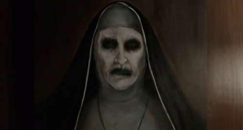 A Very Scary Nun With A Mustache Is Standing In A Dark Room . GIF