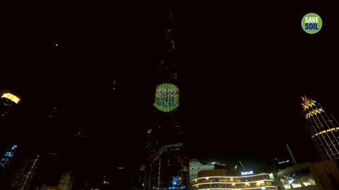 A Very Tall Building Is Lit Up At Night With A Save Soil Sticker On It GIF