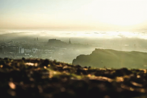A View Of A City From A Hill With The Sun Shining Through The Clouds GIF