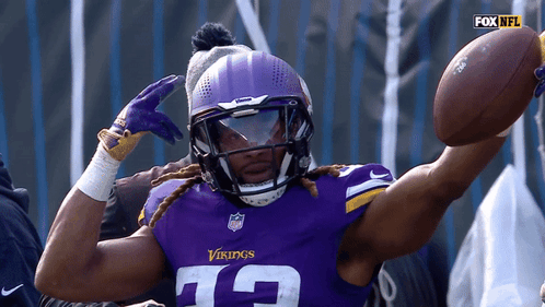 A Vikings Player Wearing A Helmet And Gloves Holds A Football GIF