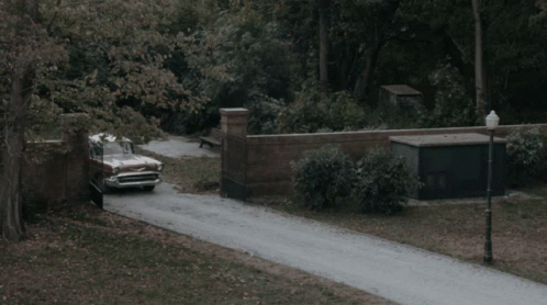 A Vintage Car Is Driving Down A Road With A Brick Wall In The Background GIF