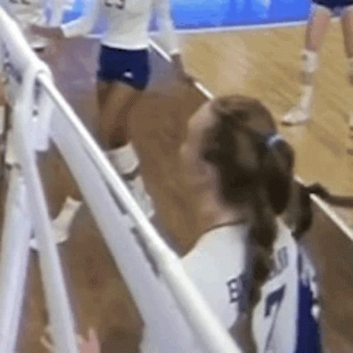 a volleyball player wearing a white jersey with the number 7 on it is standing next to a white fence .
