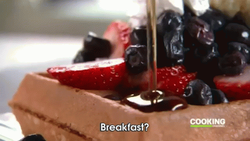 a waffle with strawberries blueberries and syrup being poured on it with the words breakfast cooking channel in the back
