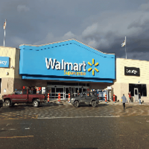 A Walmart Store With Cars Parked In Front Of It On A Cloudy Day GIF