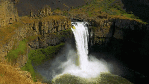 A Waterfall In The Middle Of A Canyon With A Few Trees In The Background GIF