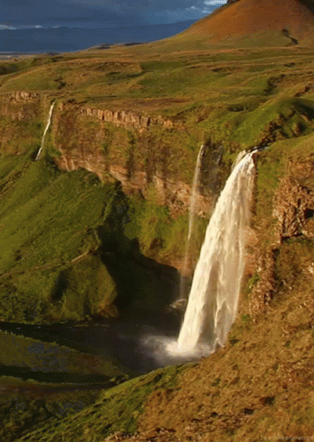 A Waterfall In The Middle Of A Grassy Valley GIF