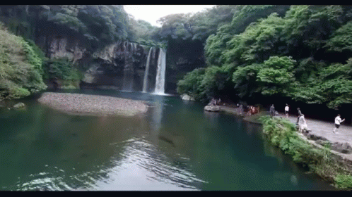 A Waterfall Surrounded By Trees And A Lake GIF