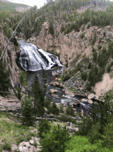 A Waterfall Surrounded By Trees And Rocks In A Valley GIF
