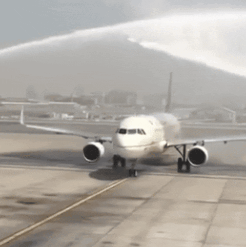 A White Airplane Is Being Sprayed With Water On The Tarmac GIF