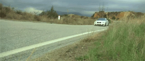 A White Bmw Is Driving Down A Road GIF