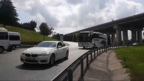 A White Bmw Is Driving Down A Road Next To A Bus That Says ' Istanbul ' On It GIF