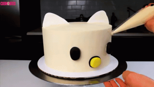 A White Cake With Black Circles And Ears Is Being Decorated By A Person GIF