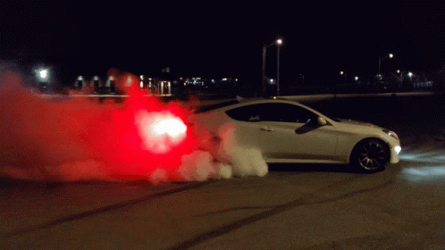 A White Car Is Doing A Burnout At Night With Red Smoke Coming Out Of The Back GIF
