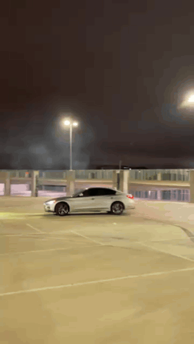 A White Car Is Doing A Stunt In A Parking Lot At Night GIF