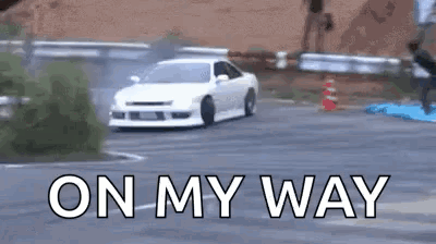 A White Car Is Drifting Down A Road With The Words `` On My Way '' Written On The Bottom . GIF